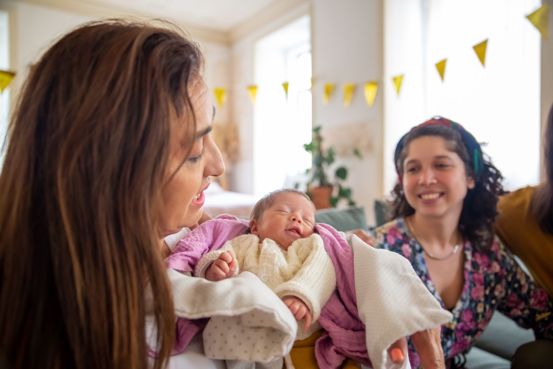 A mother holding her newborn baby during a family celebration, reflecting a modern baek-il gathering