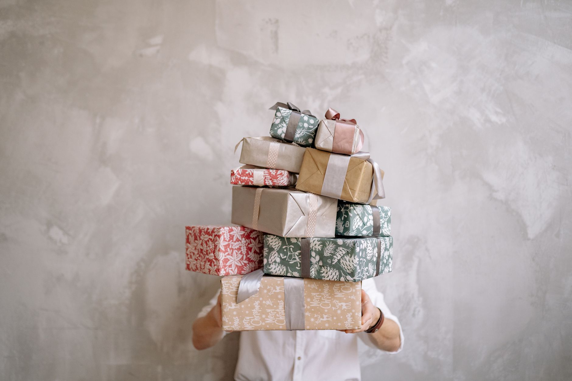 Person holding a large stack of wrapped holiday gift boxes