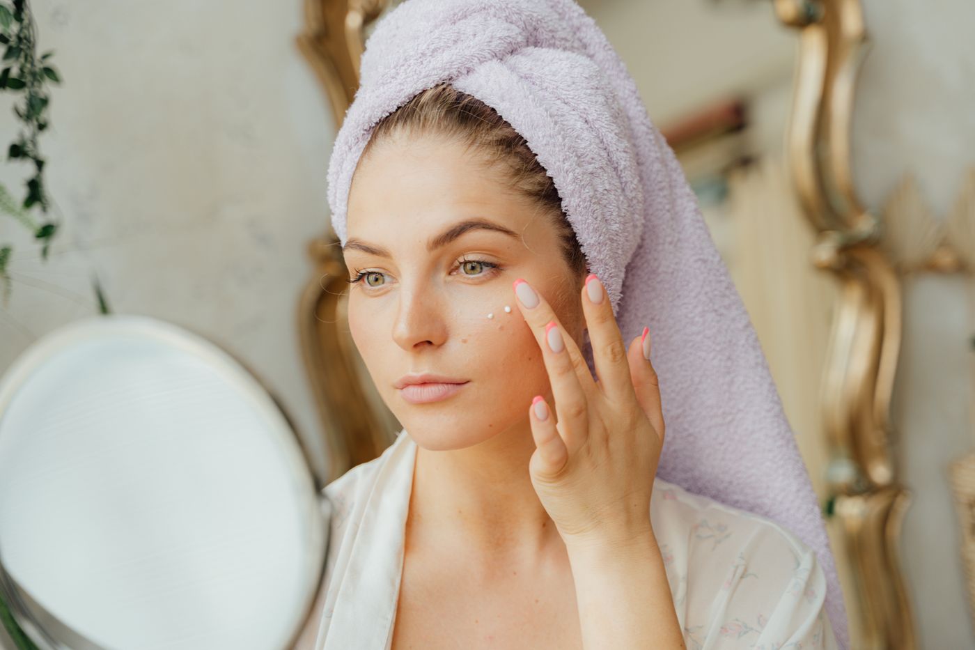 Woman applying moisturizer in front of a bathroom mirror as part of a skincare routine