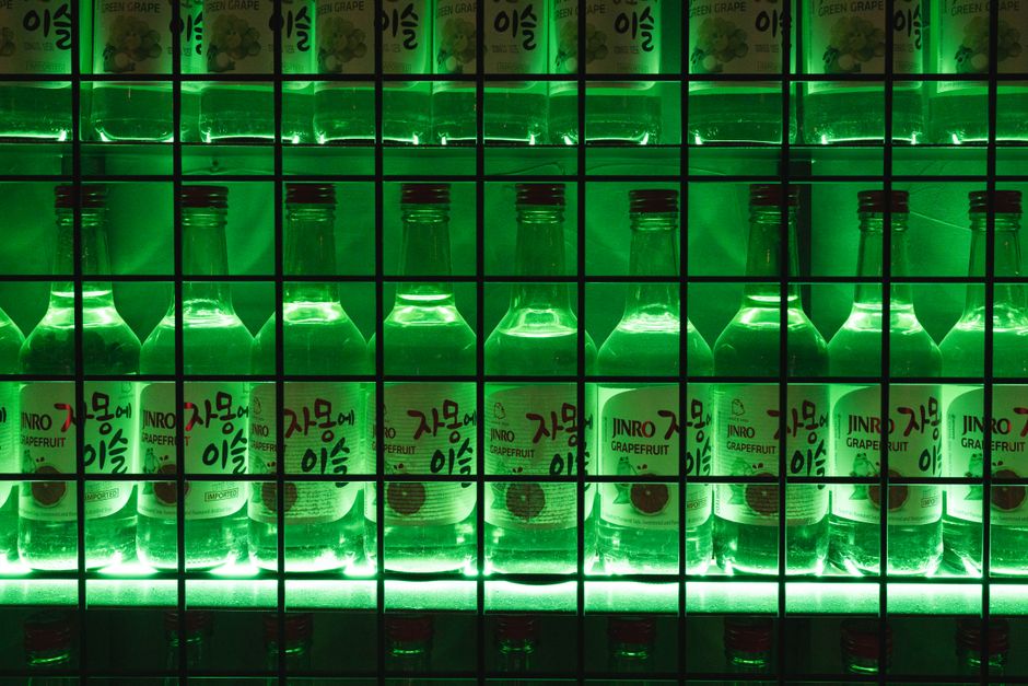 Rows of Jinro soju bottles lit up green on a bar shelf in Korea
