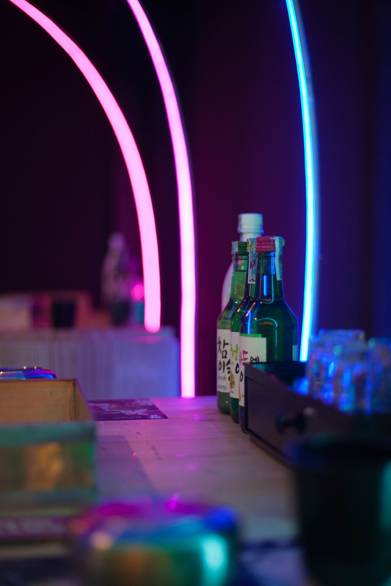 Colorful soju bottles lined up on a bar counter under neon lighting