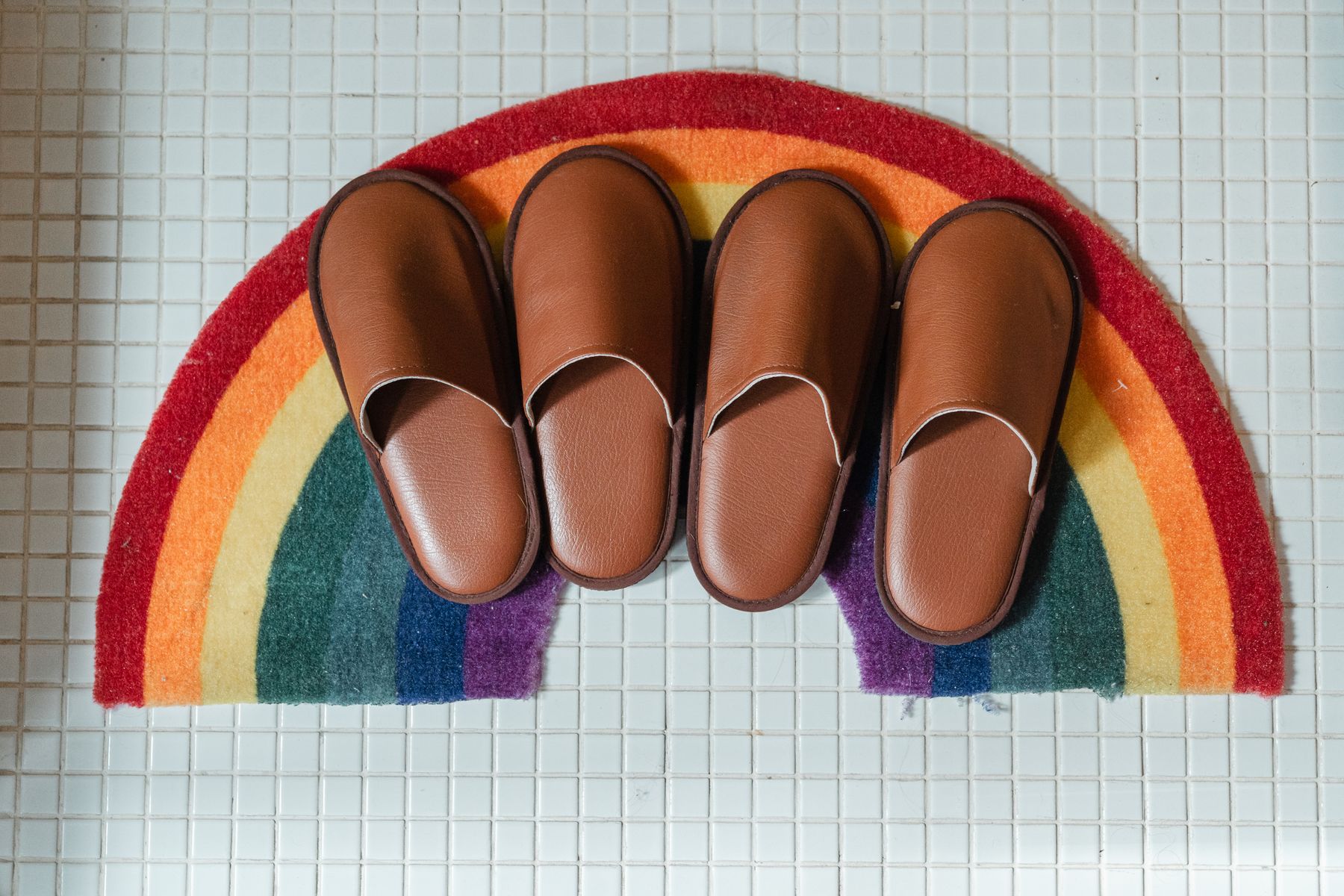 Pair of bathroom slippers sitting on a white tiled bathroom floor near the entrance