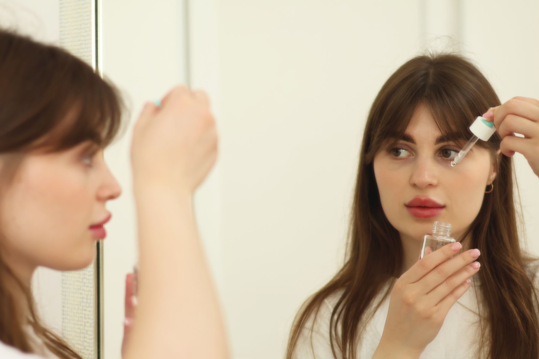 Woman applying a lightweight skincare serum in front of a mirror as part of a nightly routine