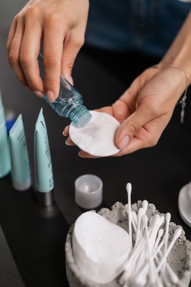 Close-up of hands applying toner to a cotton pad during a skincare routine