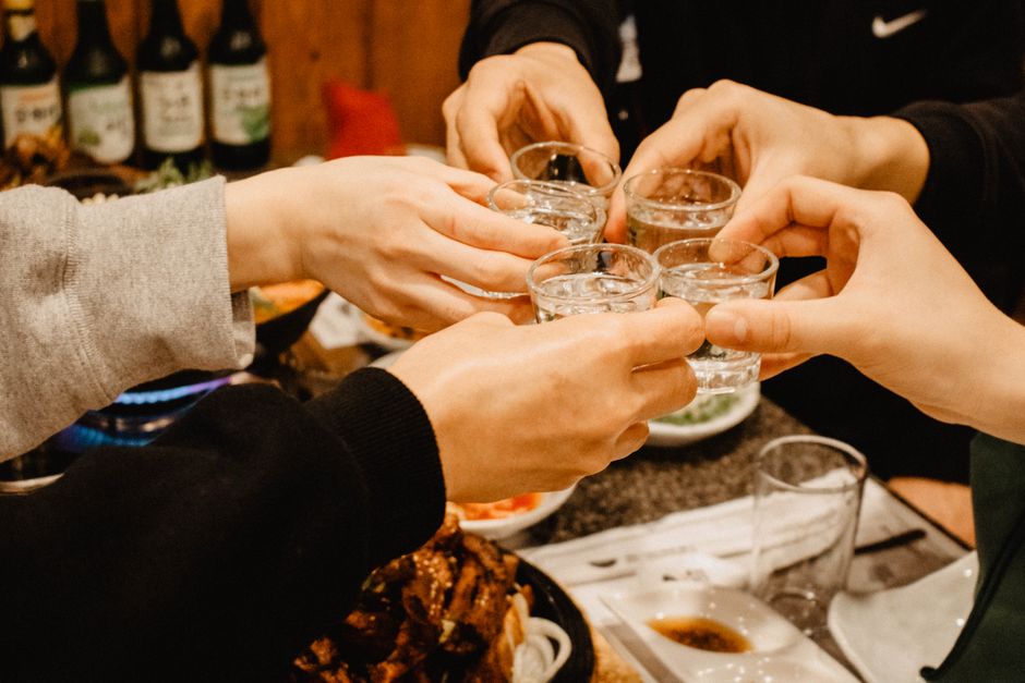 A group of friends clinking glasses together during a toast at a Korean dinner table