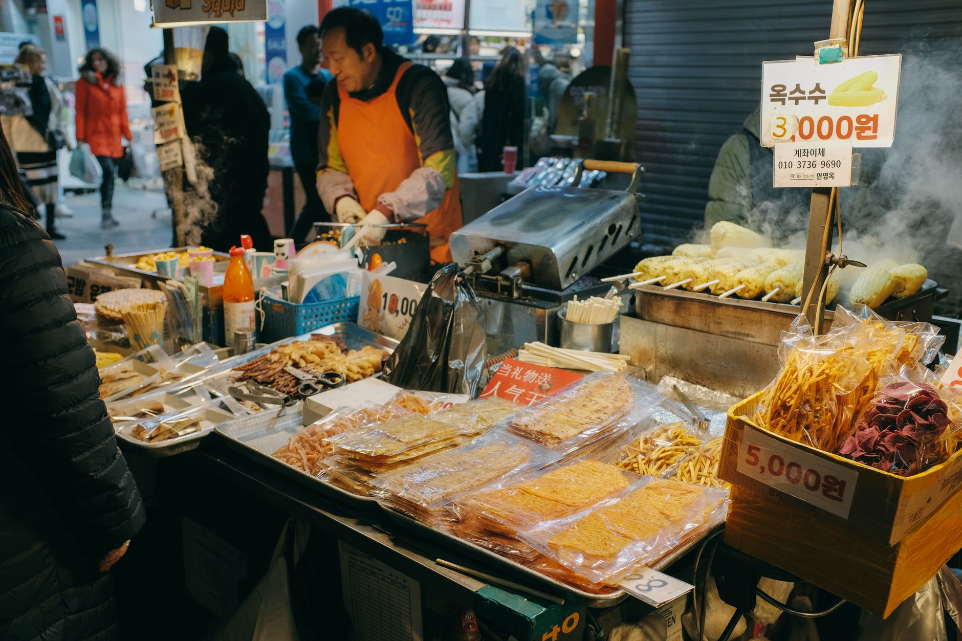 A bustling street food alley in Seoul with vendors preparing Korean snacks