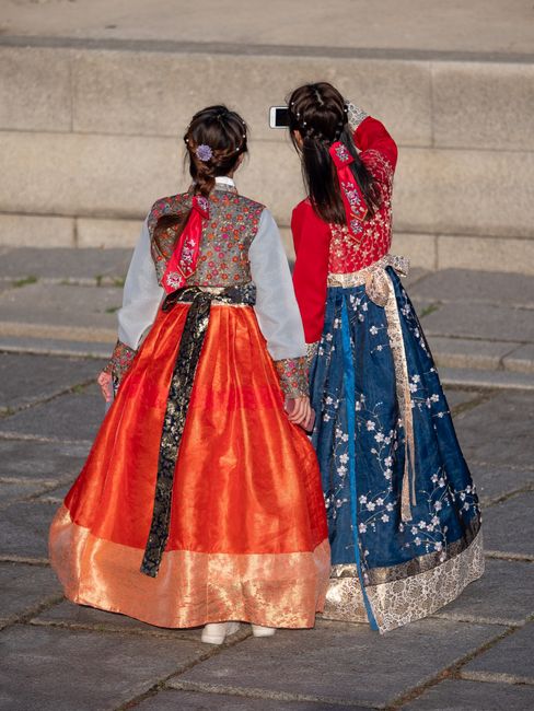 Two women in colorful traditional hanbok walking through a palace courtyard in Seoul